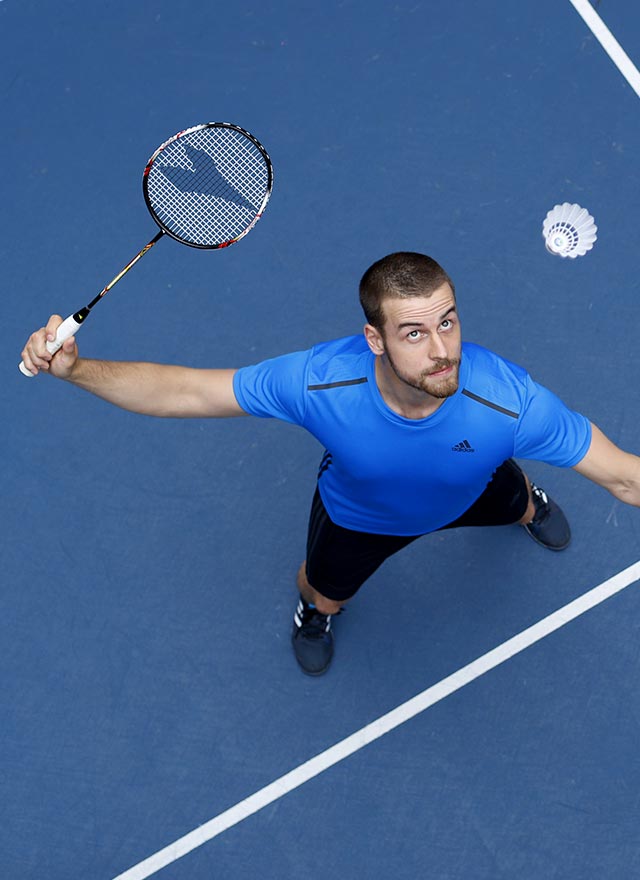 Homme qui joue au badminton et qui porte un tshirt Adidas bleu